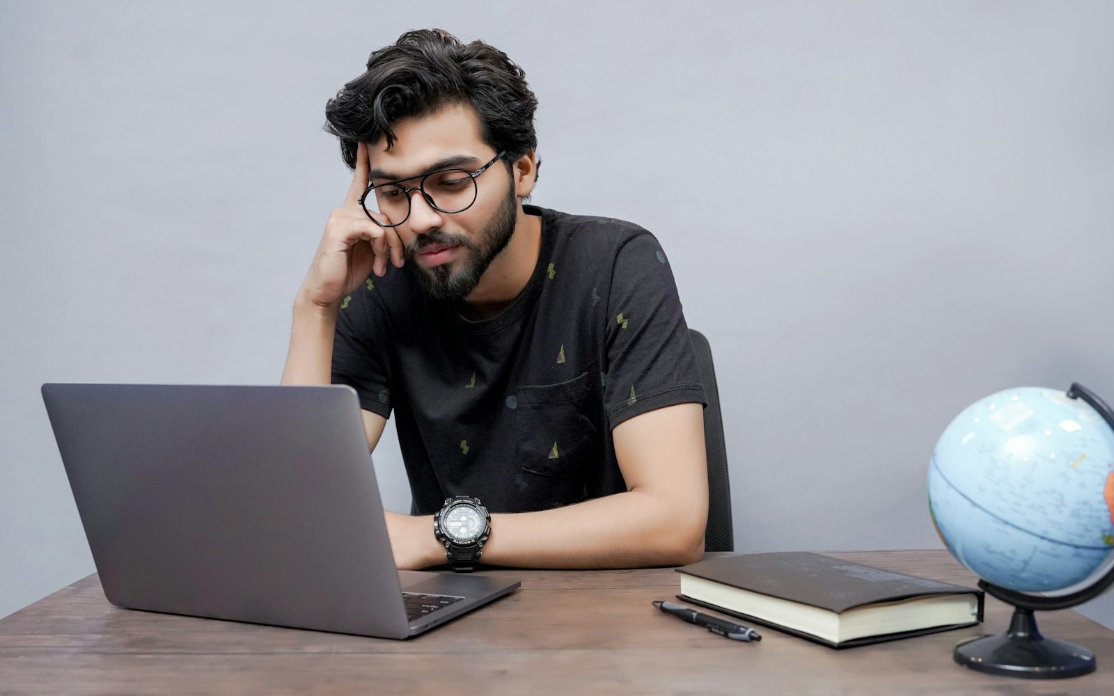 Focused Indian student thinking while working on a laptop